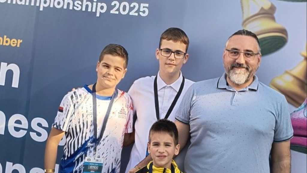 Mladi šahisti pokazuju medalje pored organizatora